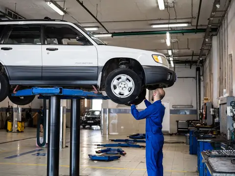 A technician working under a raised white SUV in a bright shop